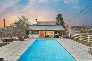 Una piscina rectangular con superficie de agua azul cristalina, rodeada por una zona de patio pavimentada con mobiliario exterior y una zona de estar cubierta.