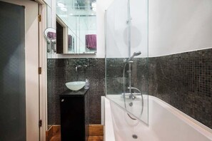 A modern bathroom with a glass-enclosed shower, a white bathtub, and a black vanity with a bowl sink. - Unique 2 Bed Chelsea townhouse | BeeMyGuest® (London)