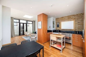 A modern kitchen with a wooden cabinet, a stove, and a dining area with a table and chairs. - Unique 2 Bed Chelsea townhouse | BeeMyGuest® (London)