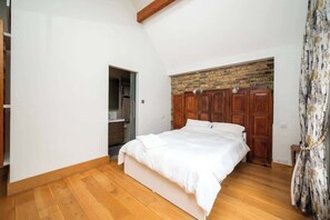 A bedroom with a wooden floor, a bed with white bedding, a wooden wardrobe, and a brick accent wall. - Unique 2 Bed Chelsea townhouse | BeeMyGuest® (London)