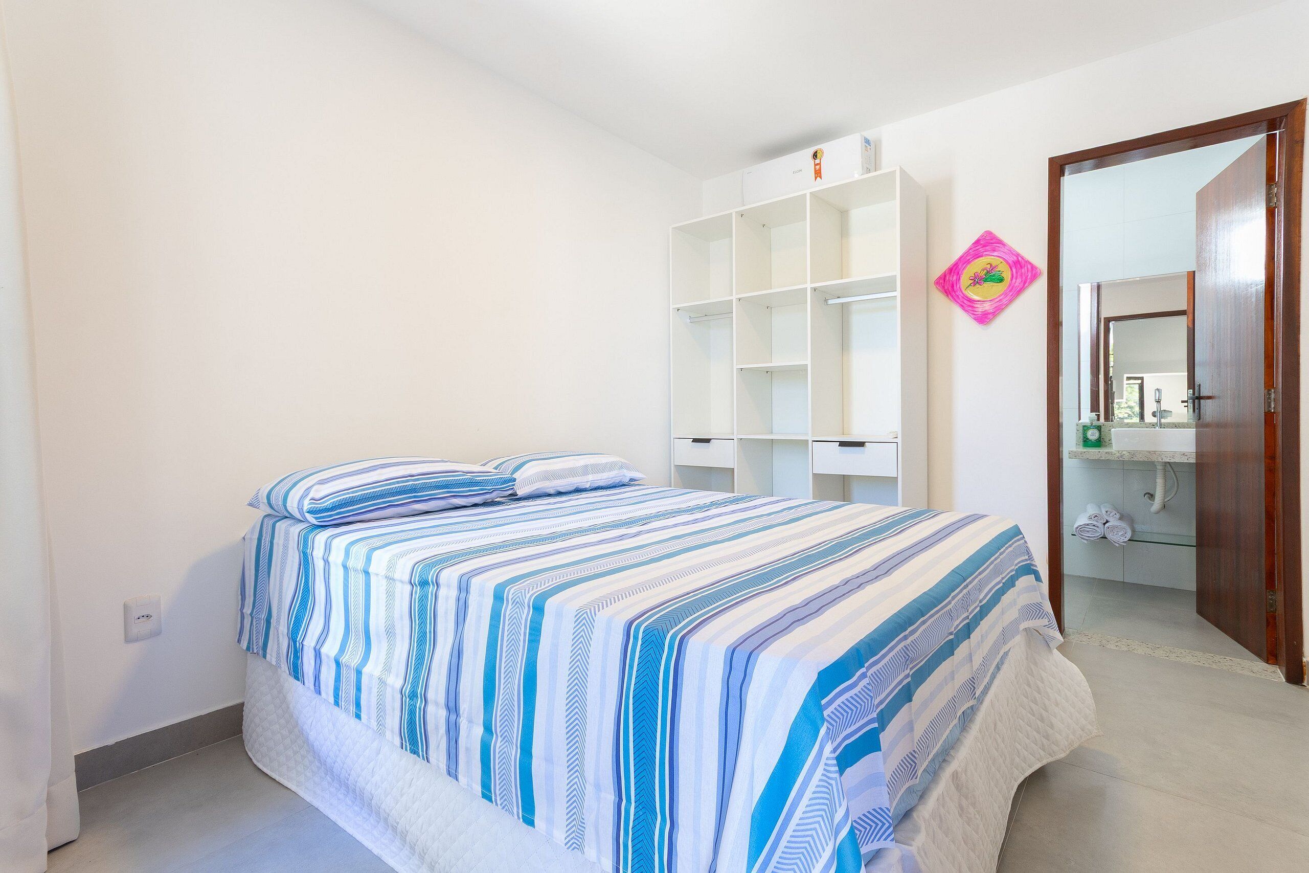 Camera da letto con un letto, un armadio bianco, un bagno parzialmente visibile attraverso una porta aperta e un elemento decorativo rosa al muro.