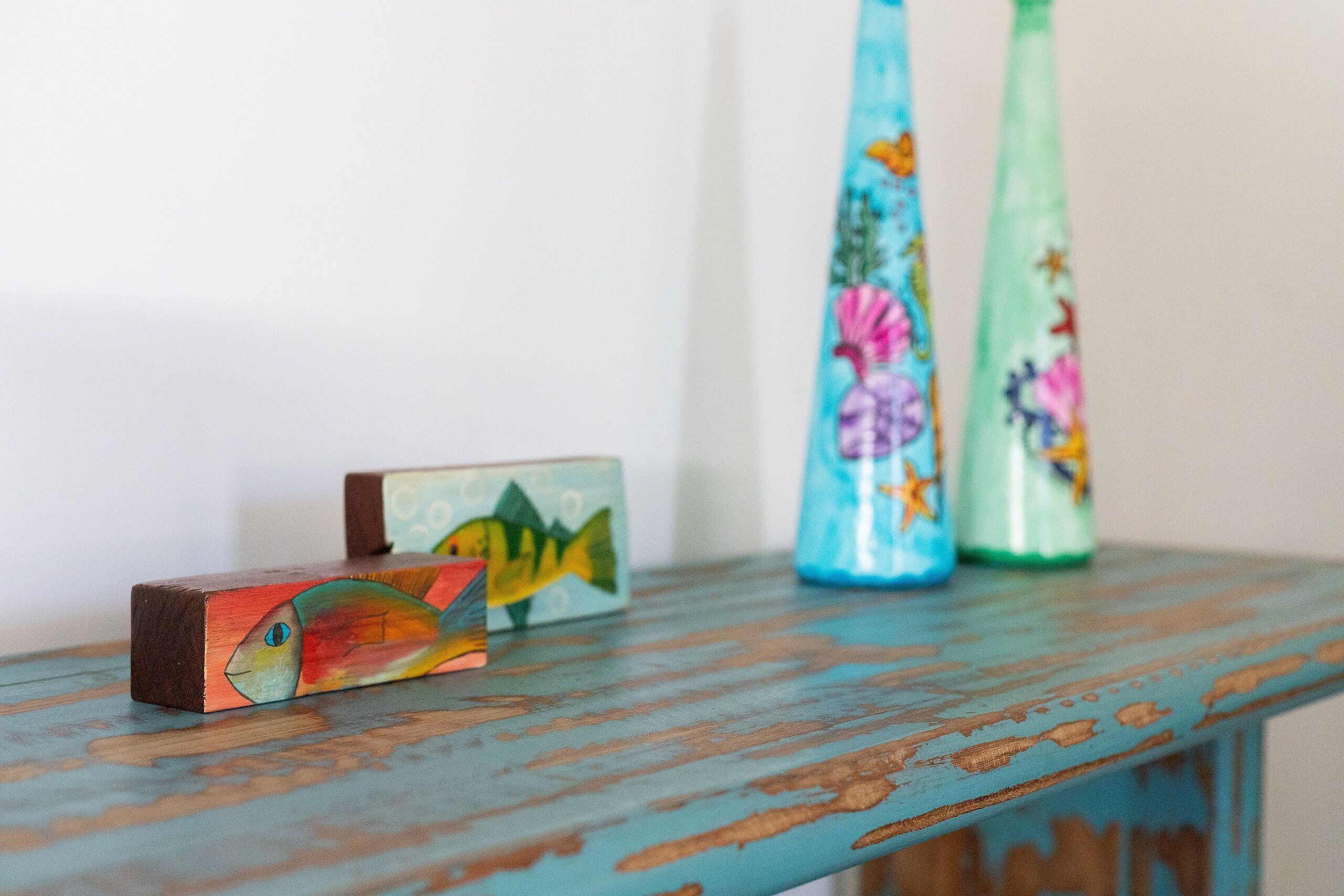 A wooden shelf with a painted fish, two decorated bottles, and a small block.