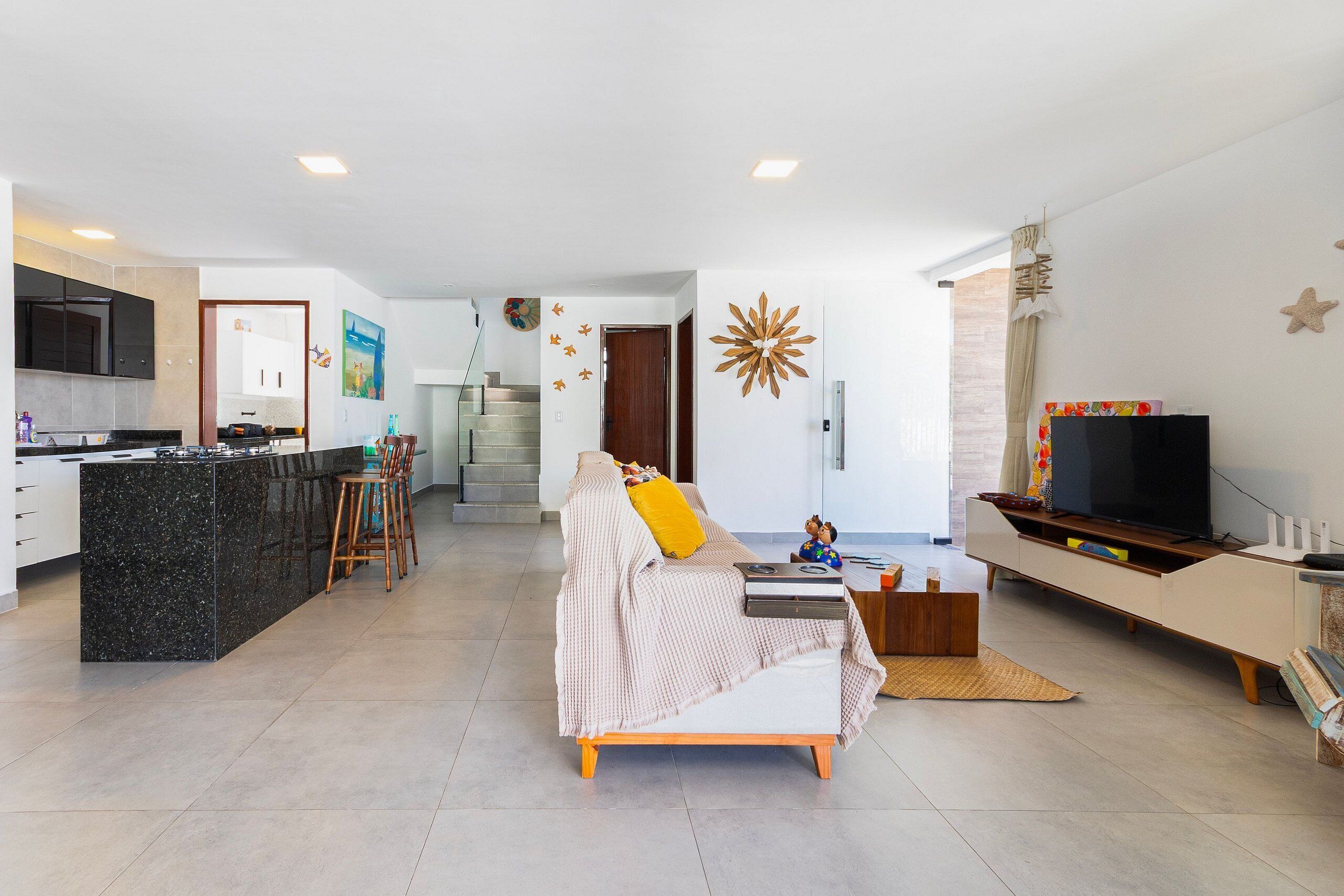 Un espacio habitable moderno con cocina, sofá, televisor y una escalera.