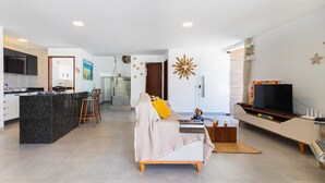 A modern living space with a kitchen, a sofa, a TV, and a staircase. - Altos do Caju - Triplex in Pirangi 300 Meters From the World's Largest Cashew Tree by Carpediem (Parnamirim)