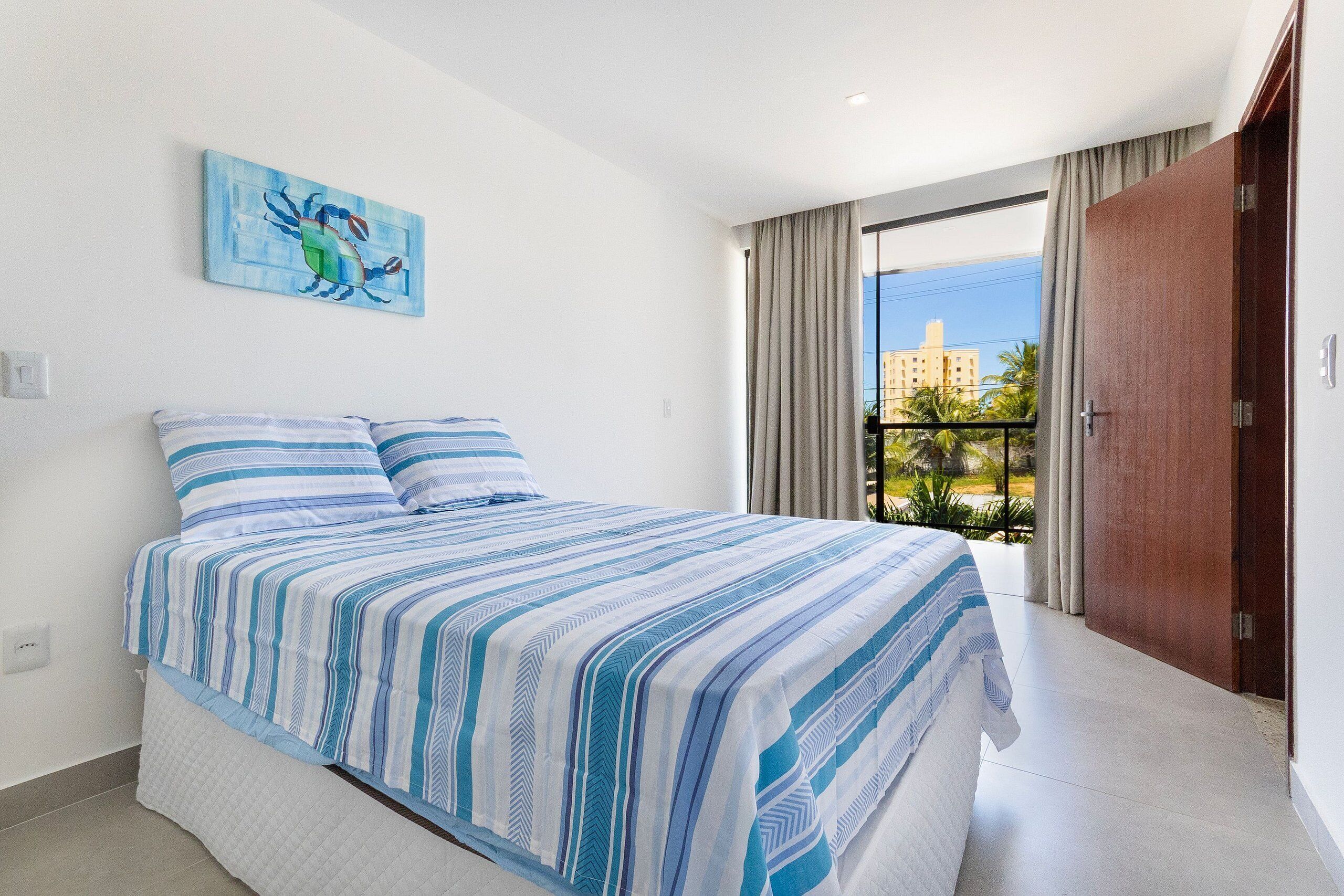 Un dormitorio con cama, un cuadro, una ventana con cortinas y vistas a edificios.