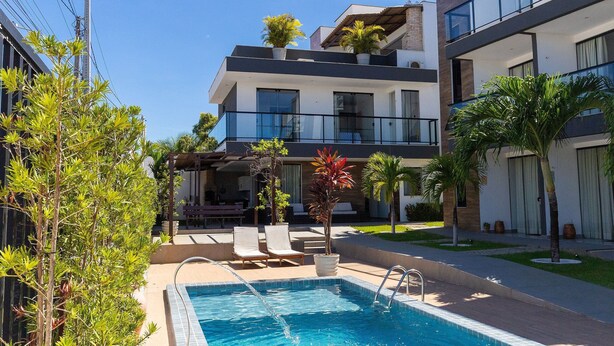 A modern building with a pool, lounge chairs, and potted plants. - Altos do Caju - Triplex in Pirangi 300 Meters From the World's Largest Cashew Tree by Carpediem (Parnamirim)