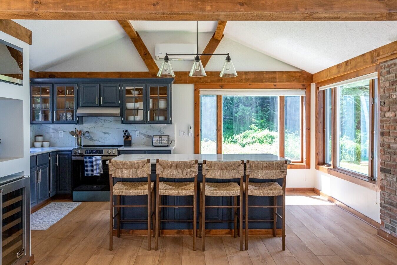 A modern kitchen with dark cabinets, a marble countertop, and a dining area with wicker chairs.