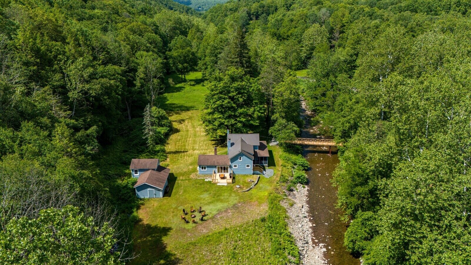 Une maison à deux étages avec un porche à l’avant, un petit garage séparé et une rivière qui la borde.