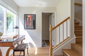 Eine Treppe mit Holzboden und Handlauf, ein Schreibtisch mit Lampe, ein Poster an der Wand und ein Blick ins Freie durch ein Fenster.