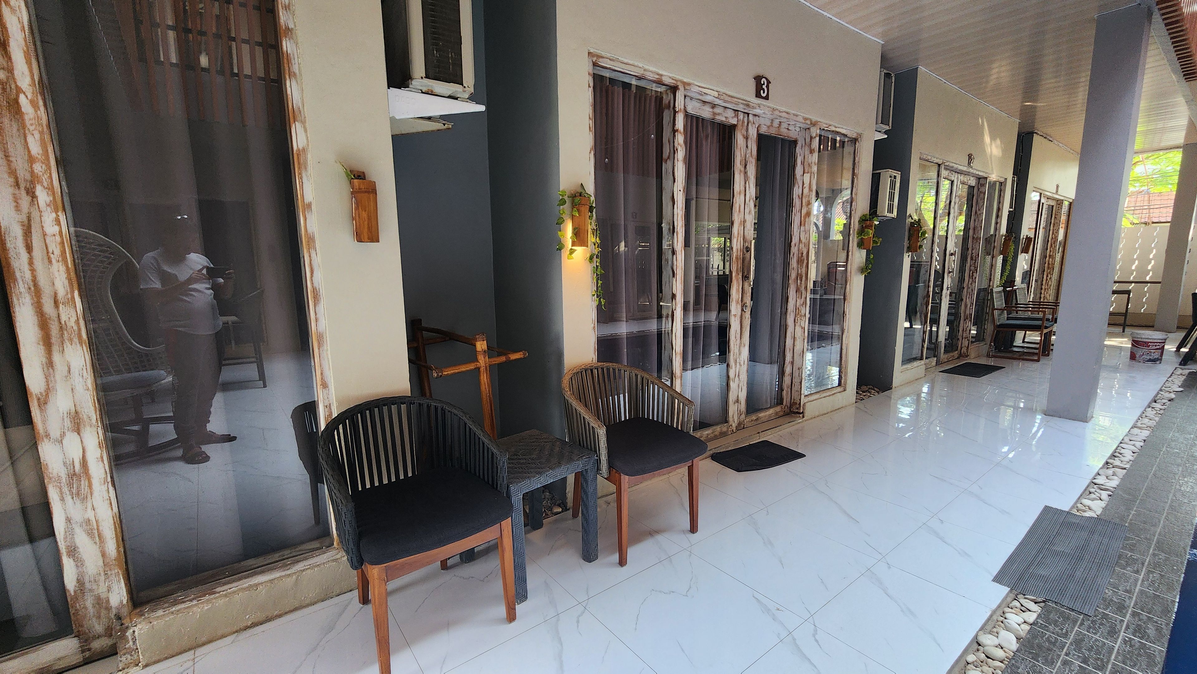 A covered outdoor area with two chairs, a bench, and a tiled floor.