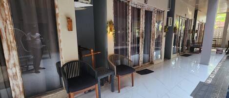 A covered outdoor area with two chairs, a bench, and a tiled floor.