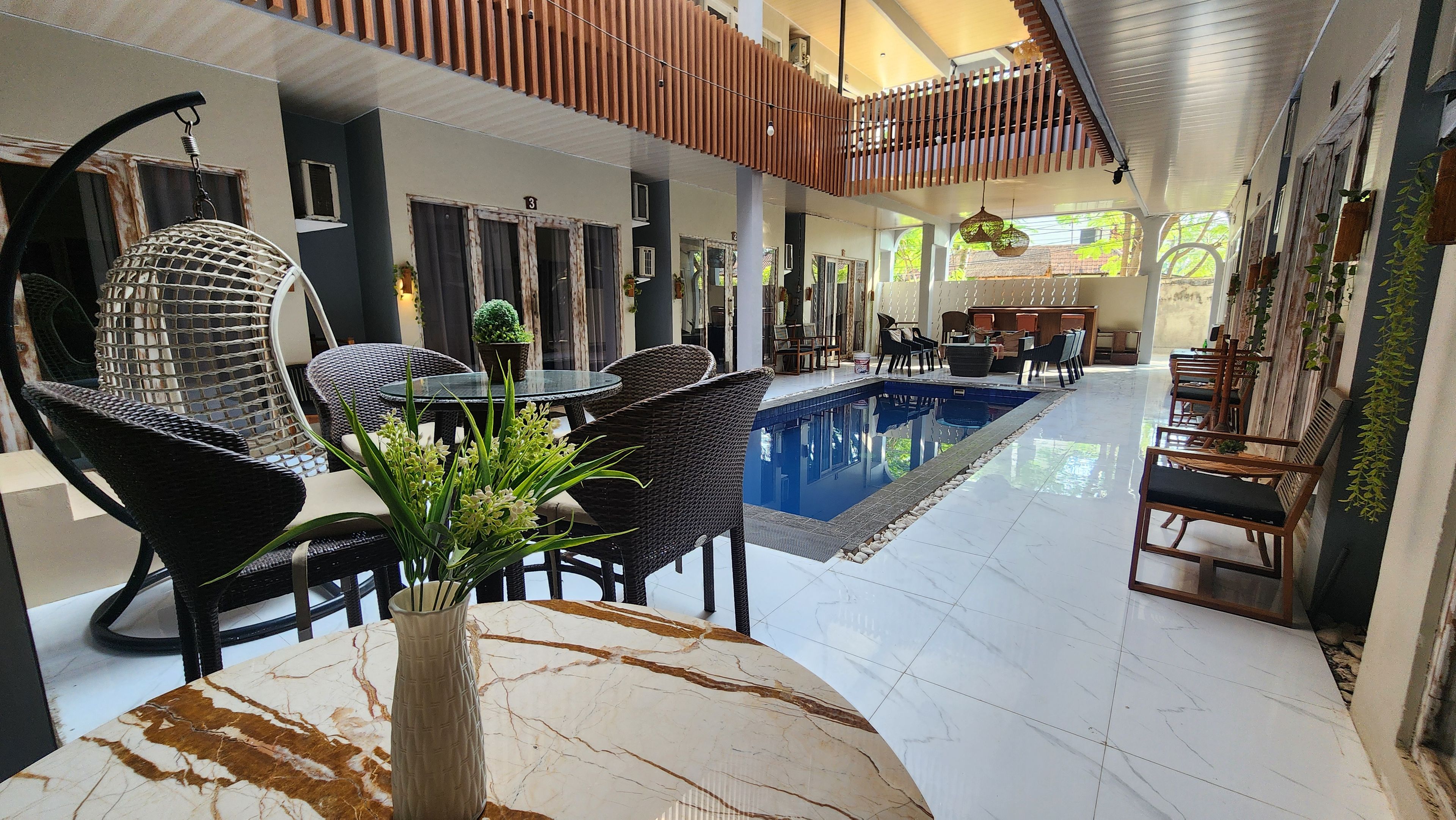 Un hall d’hôtel avec une piscine, des meubles en osier et une table en marbre.