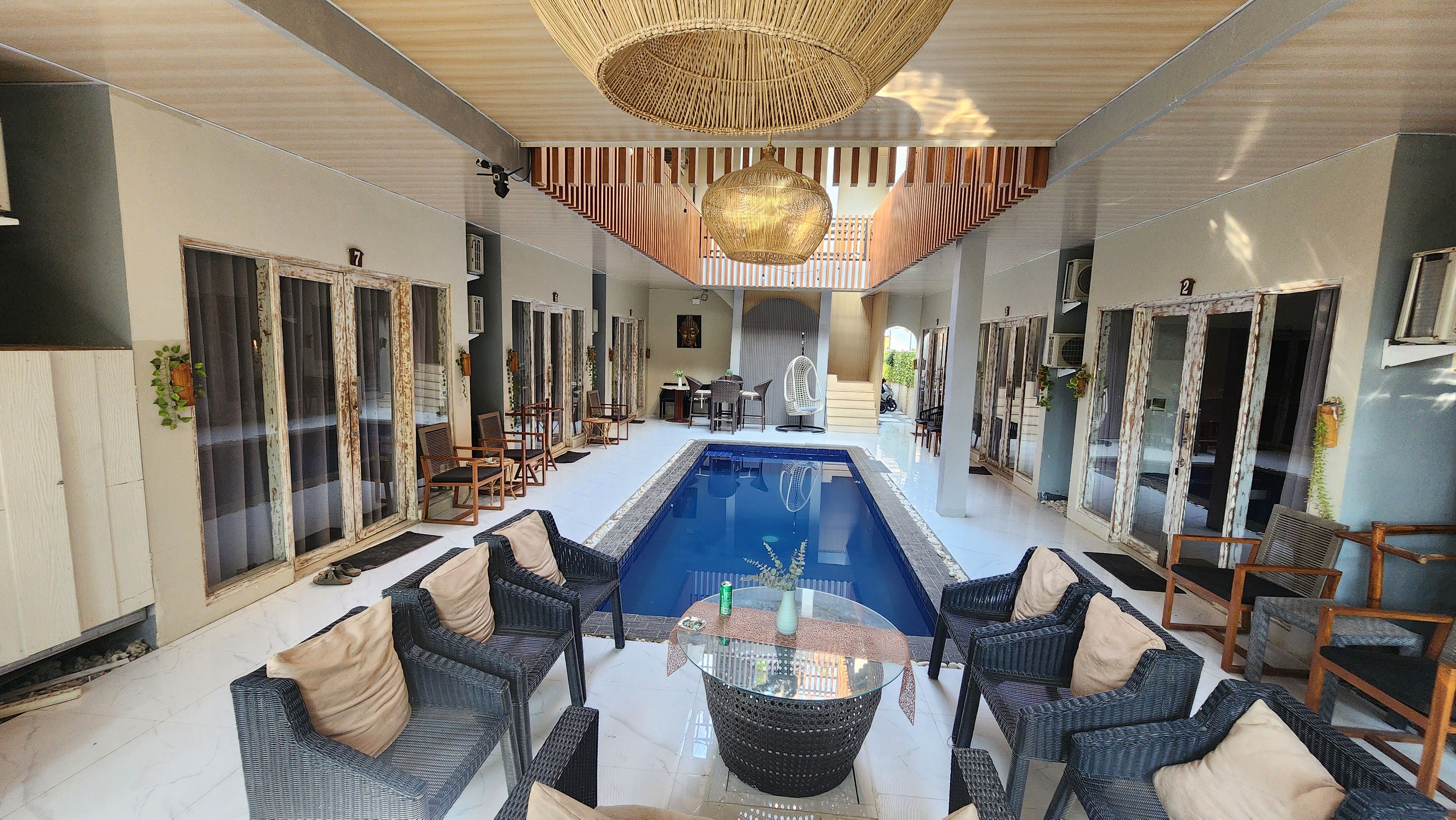 A pool area with wicker furniture and a glass table, surrounded by doors and a staircase.
