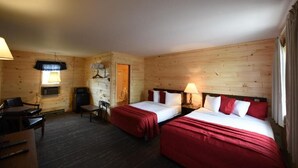 A wooden cabin room with two beds, a desk, a chair, a lamp, and a small table.