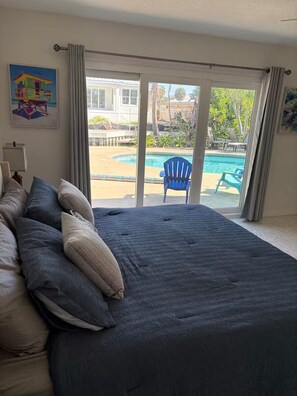 Ein Schlafzimmer mit einem großen Bett, Blick auf einen Swimmingpool und einem Balkon.