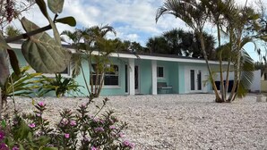 A building with a light blue exterior, surrounded by a gravel driveway and various plants. - Siesta Key Village Home (Siesta Key)