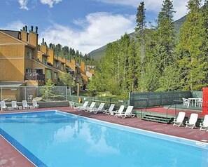 A swimming pool with lounge chairs, a red safety fence, and a mountainous backdrop.