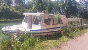 Un barco estacionado con cabina, número de registro LY F63367 F, amarrado cerca de una ribera cubierta de hierba con un sendero a su lado.