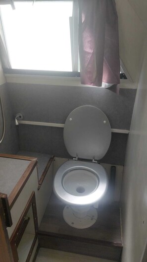 Une petite salle de bain comprenant des toilettes, une fenêtre avec un rideau et un espace douche.