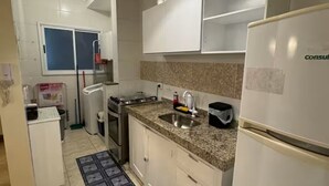 A kitchen with white cabinets, a granite countertop, a stainless steel sink, a refrigerator, and a red pendant light. - Casa Melo 8 - Ubatuba (Ubatuba)