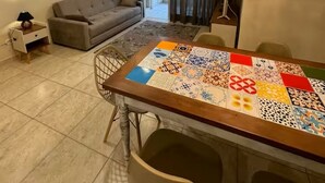 A living room with a sofa, a dining table with a colorful tablecloth, a ceiling fan, and a chandelier. - Casa Melo 8 - Ubatuba (Ubatuba)
