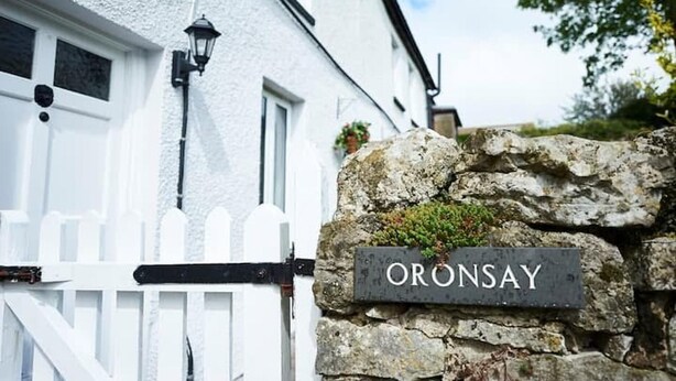 Un edificio blanco con un muro de piedra y un letrero que dice 'ORONSAY'.