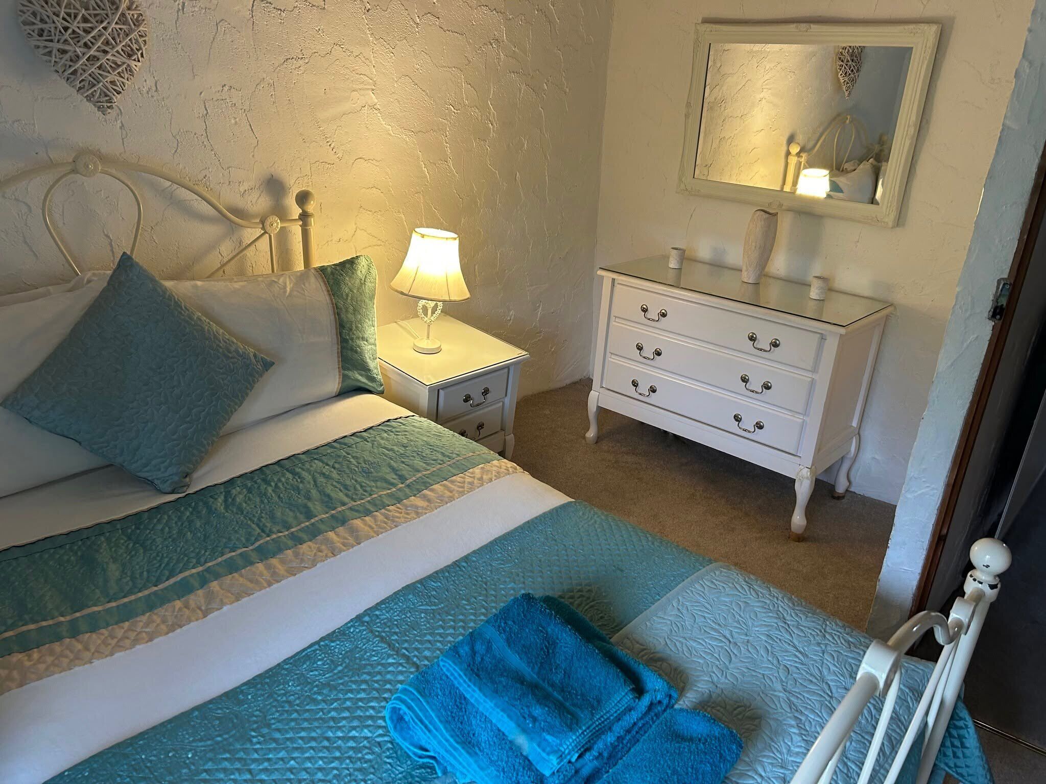 Ein Schlafzimmer mit Bett, Nachttisch, Kommode, Spiegel und Handtuch.