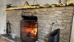 Una chimenea de piedra con fuego, una mesa de madera y un barril negro.