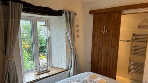 Un dormitorio con cama, ventana con cortinas, una puerta de madera y un perchero para toallas.