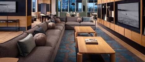 A modern living room with a sectional sofa, wooden coffee tables, and large windows offering a view of the city.