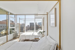 A bedroom with a large window, a four-poster bed, and a view of the cityscape.