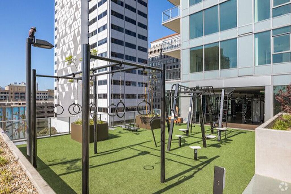 Un gimnasio al aire libre con equipo de ejercicios, rodeado por un edificio con ventanas amplias y un jardín en la azotea.