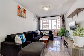 A living room with a sofa, a coffee table, a TV, and a potted plant. - Ocean Breeze San Eugenio (Costa Adeje)