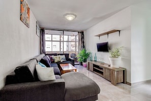 A living room with a sofa, coffee table, TV, and plants. - Ocean Breeze San Eugenio (Costa Adeje)