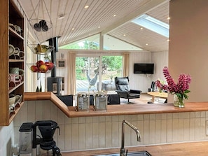 A modern kitchen with a wooden countertop, a coffee machine, and a sink. There is a seating area with a chair and a table, and a TV mounted on the wall. - Covered terrace and beach at Fjellerup (Glesborg)