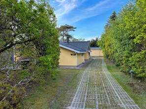 A pathway leading to a yellow building with a chimney, surrounded by trees and a clear sky. - Covered terrace and beach at Fjellerup (Glesborg)