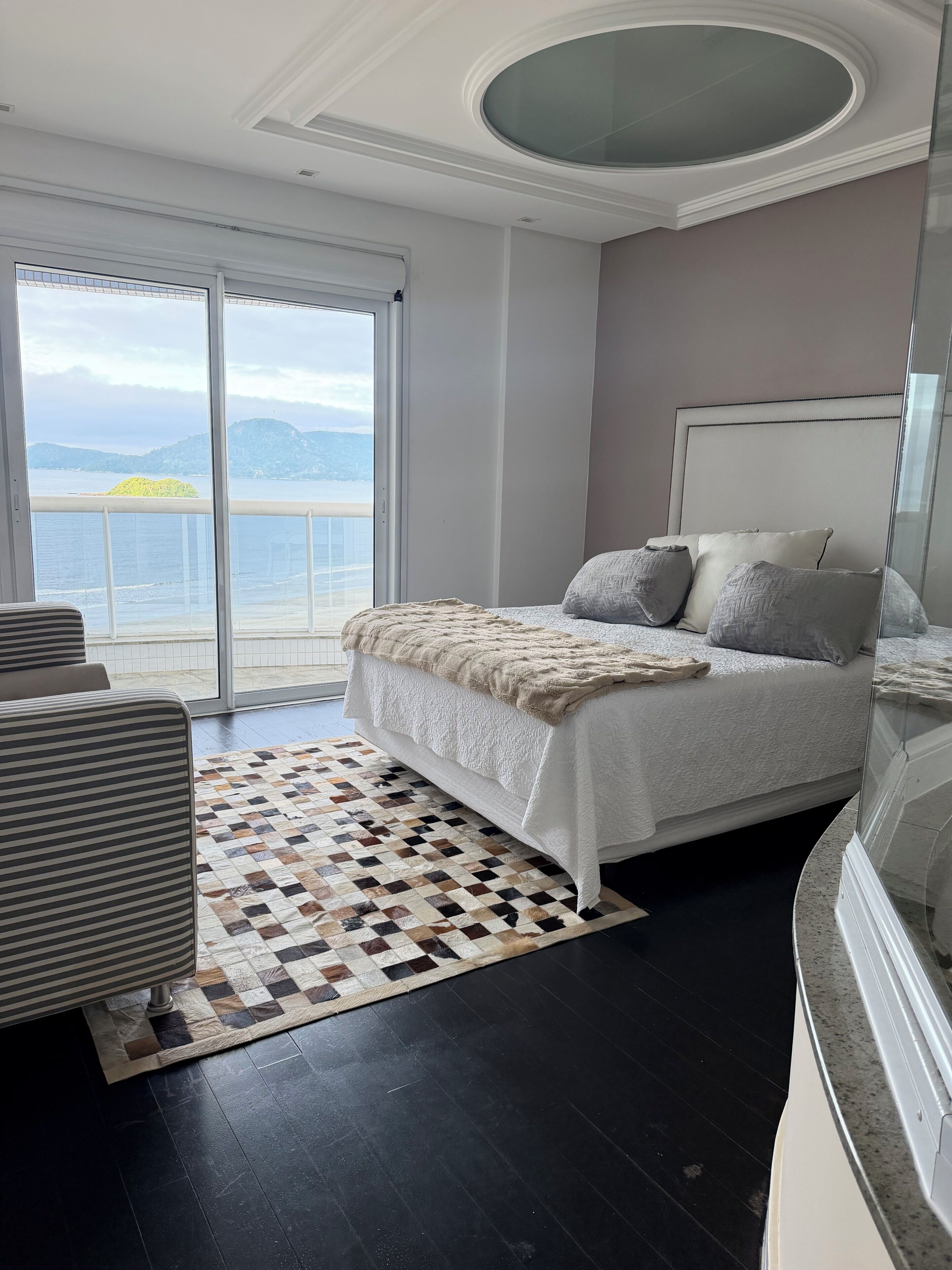 Een slaapkamer met een groot bed, een kamerkleed met dessin en uitzicht op zee door een schuifdeur.