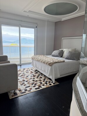 Un dormitorio con una cama grande, un tapete estampado y vistas al mar a través de una puerta corrediza.