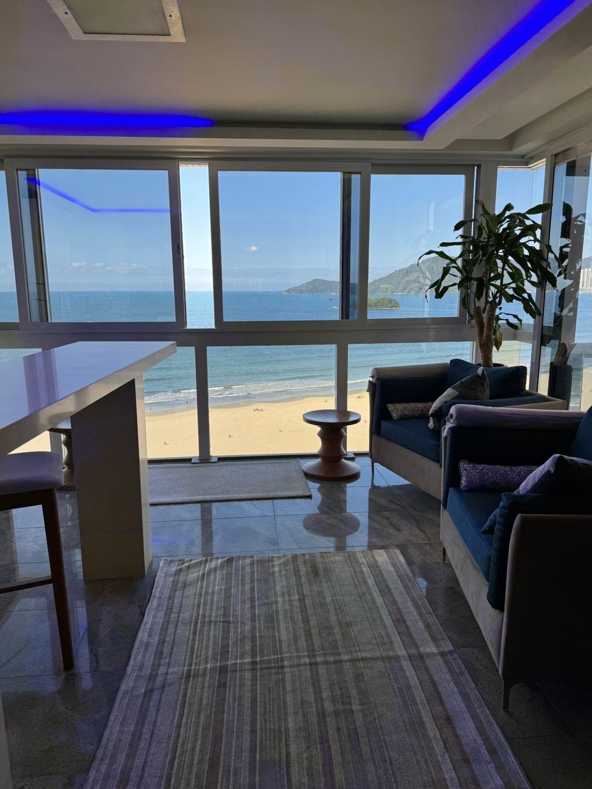 Ett rum med utsikt över stranden, en soffa, ett matbord och en krukväxt.