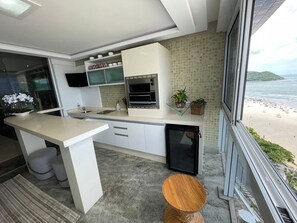 Uma cozinha moderna com forno embutido, um refrigerador pequeno e uma janela com vista para a praia.