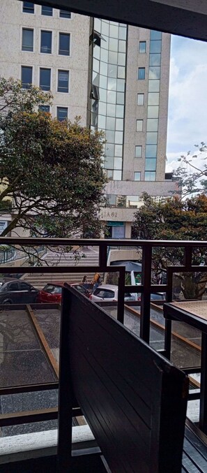 Vista de uma varanda com um edifício ao fundo, uma árvore e carros estacionados na rua.
