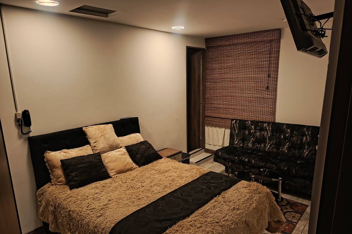 Ein Schlafzimmer mit Bett, Stuhl, einem Fenster mit Jalousien und einer Wand-Klimaanlage.