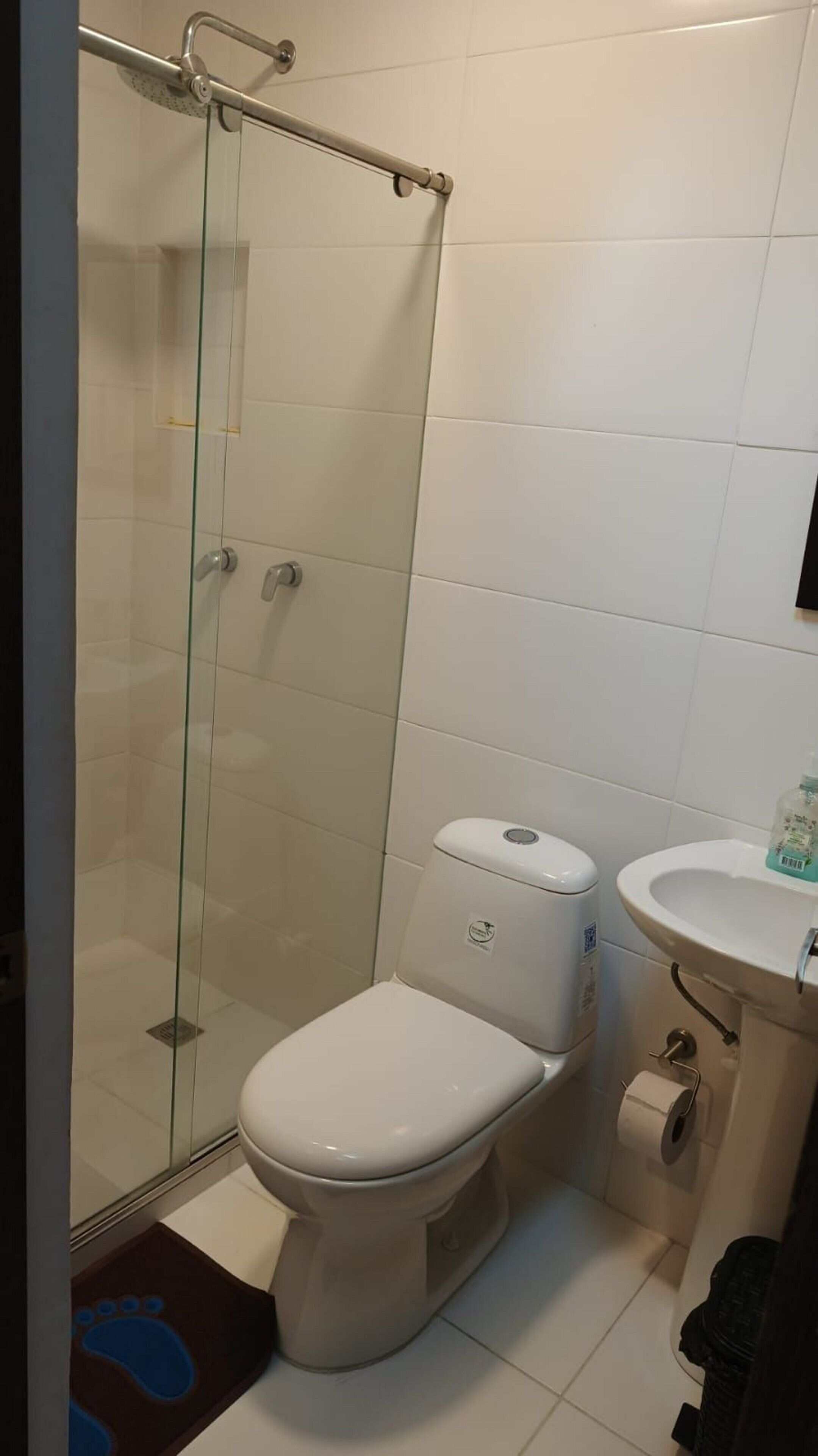 A bathroom with a glass shower enclosure, a toilet, and a sink.