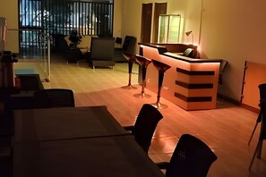 Un espacio de oficina moderno con un mostrador de recepción, dos taburetes tipo bar, una mesa de conferencias y vistas al exterior a través de amplias ventanas.