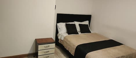 A bedroom with a bed, a bedside table with drawers, and a small rug.