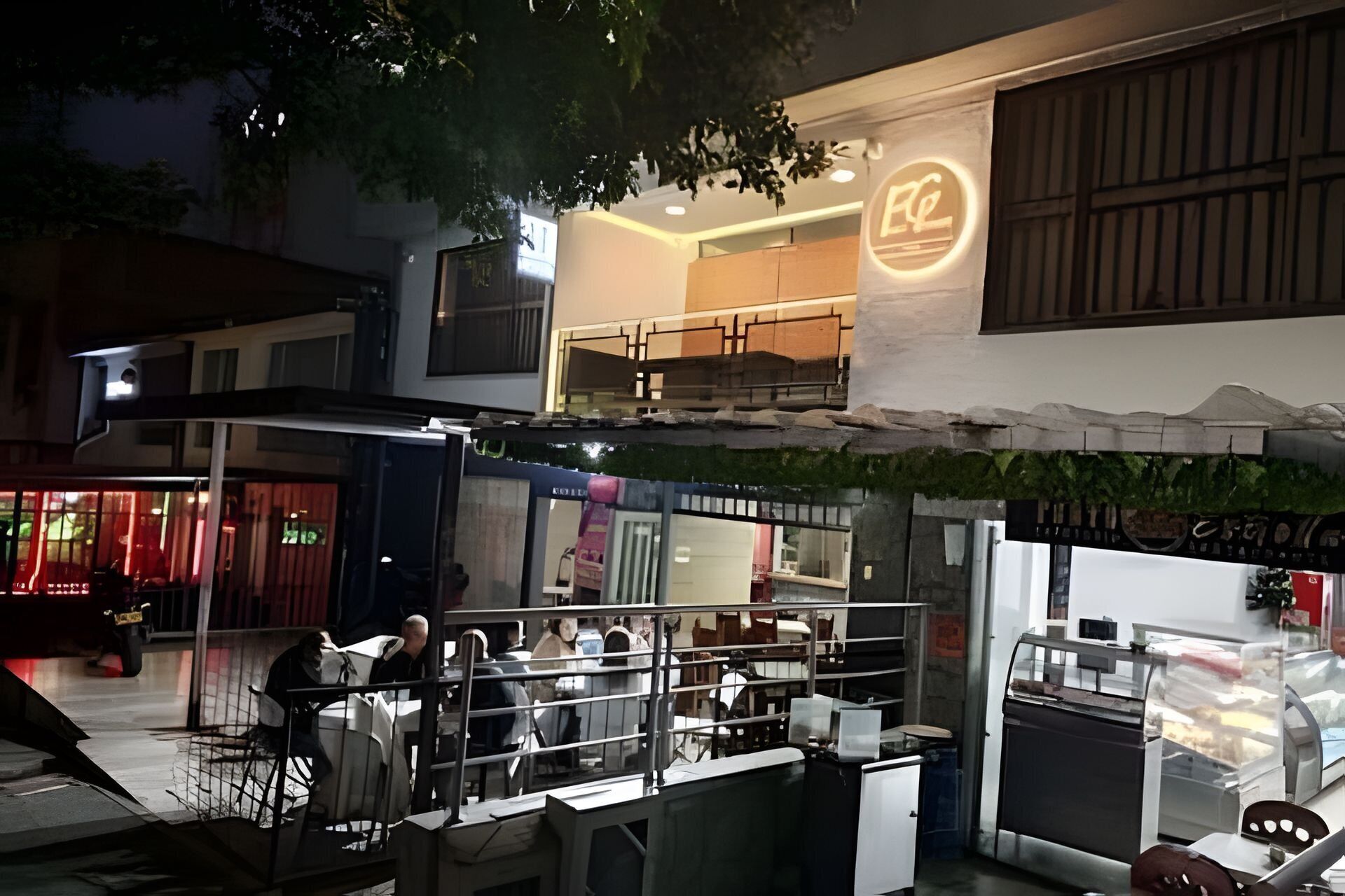 Un restaurante con terraza, una señal visible y un edificio con balcón.