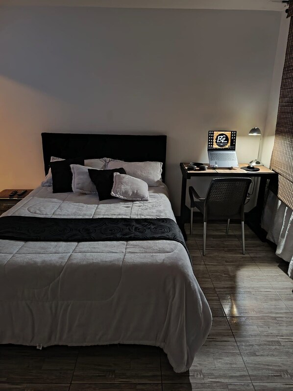 Un dormitorio ordenado con cama, escritorio y silla.