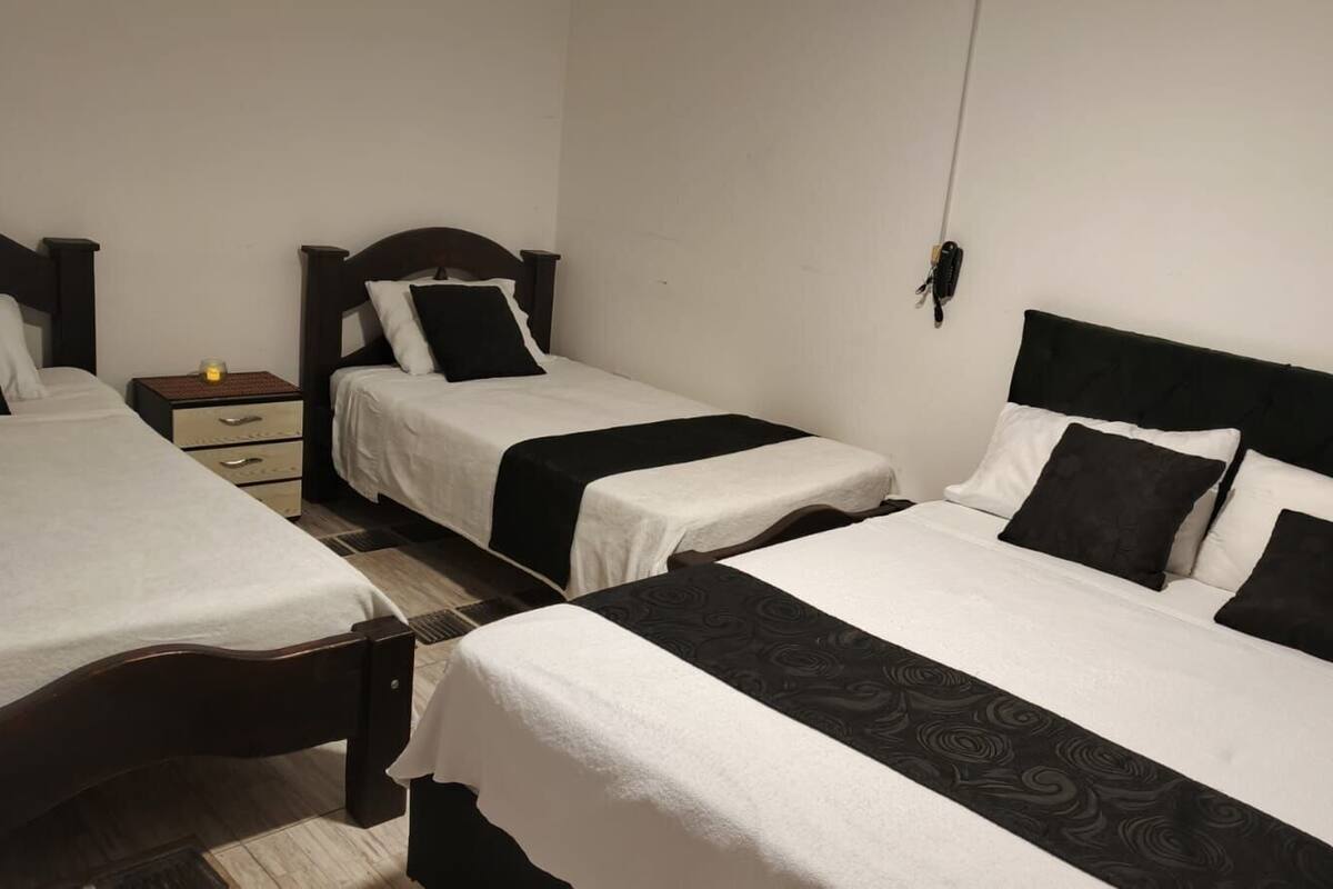 Ein Hotelzimmer mit drei Betten, jeweils mit einem hölzernen Kopfteil, einem kleinen Nachttisch und einer Lampe.