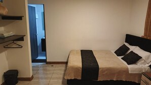 Un dormitorio con cama, una mesita de noche, un perchero y una puerta que da al baño.