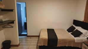 Un dormitorio con cama, una mesita de noche, un perchero y una puerta que da al baño.